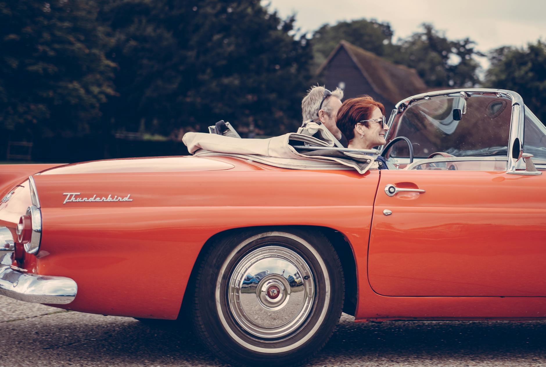 couple riding red ford thunderbird during daytime