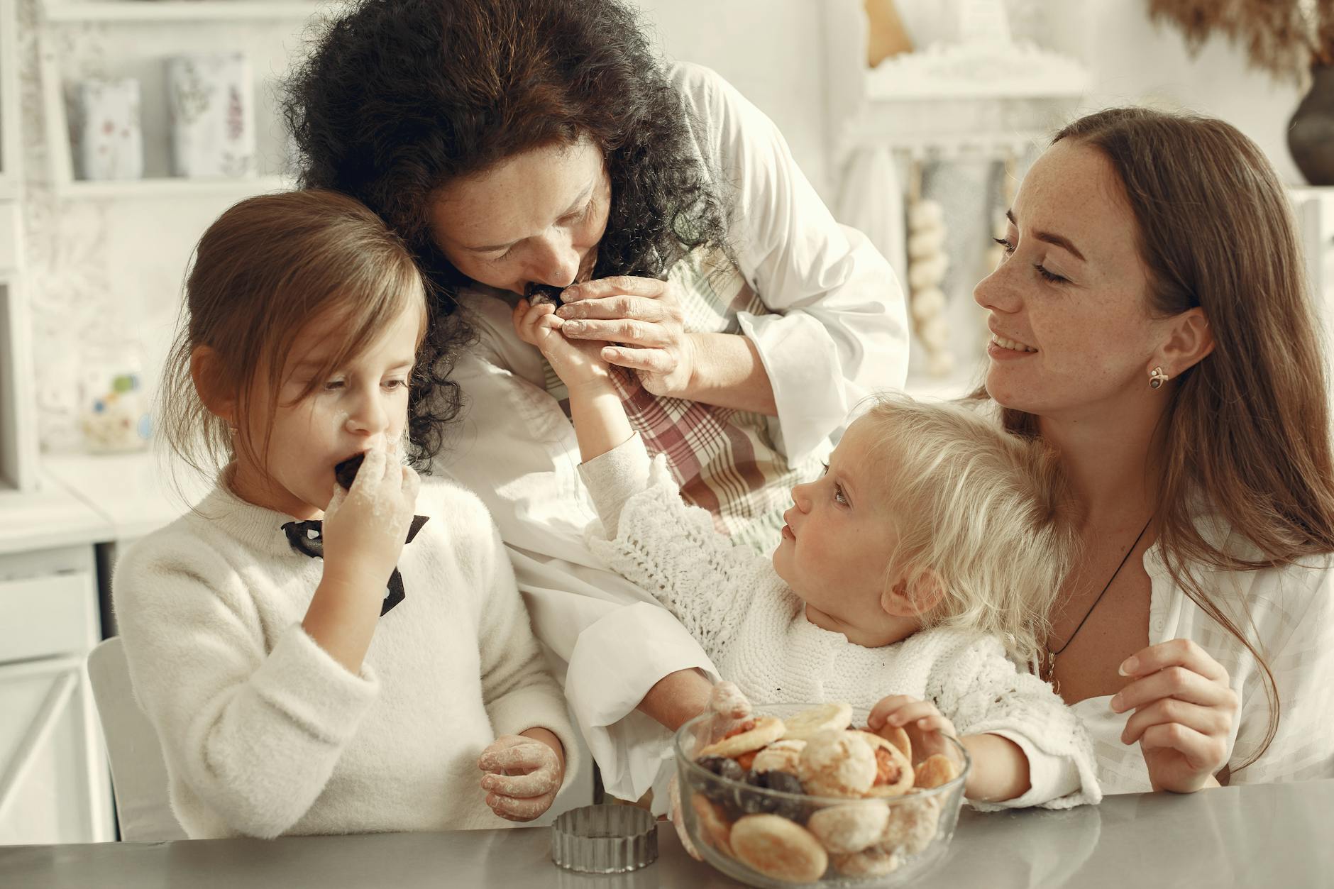 grandmother mother and two little girls in a kitchen eating cookies